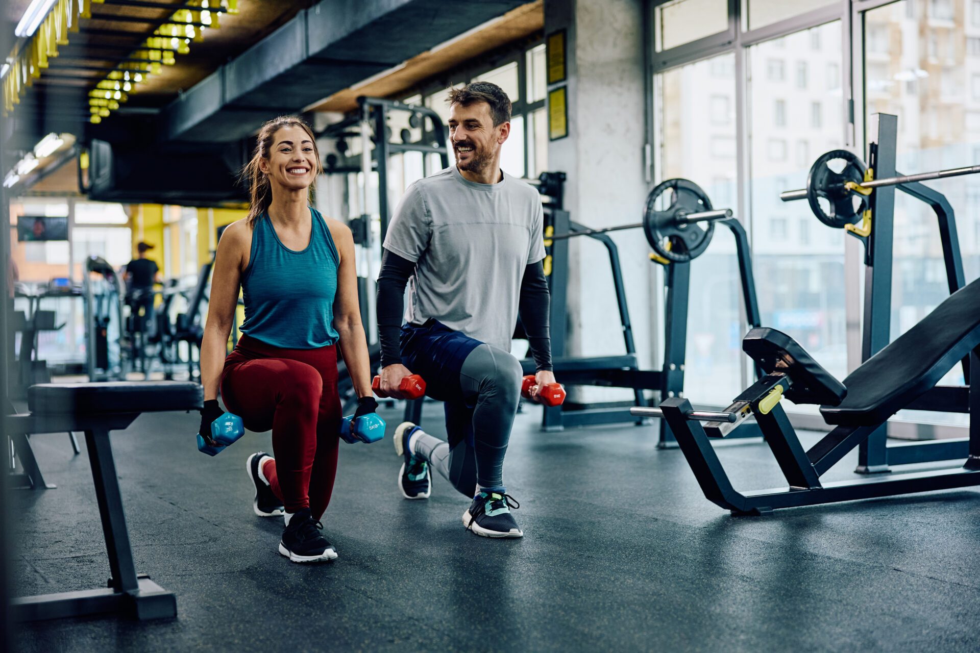 Two people training with hand weights in a bright gym